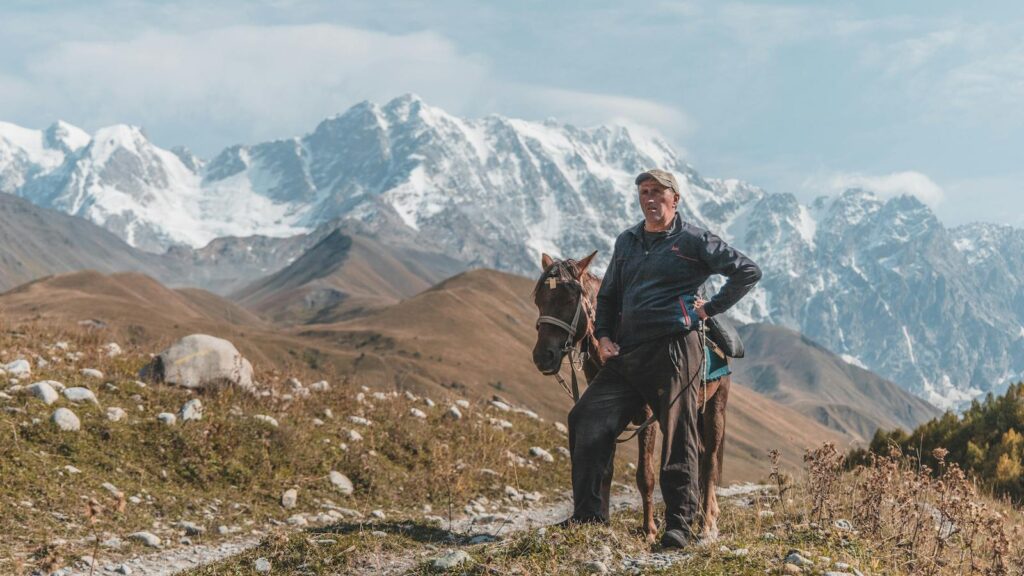A man stands with his horse against a stunning snowy mountain backdrop.