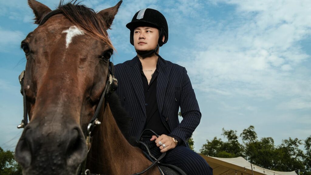 Man in helmet riding a brown horse under blue sky, showcasing equestrian style and outdoor adventure.