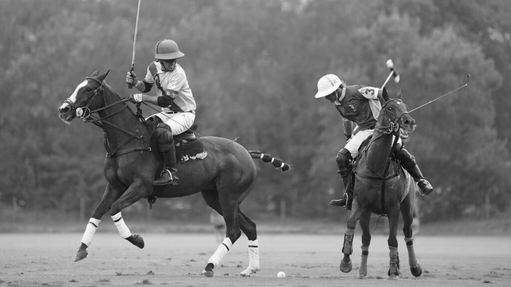Two polo players in action during an outdoor match, captured in black and white.