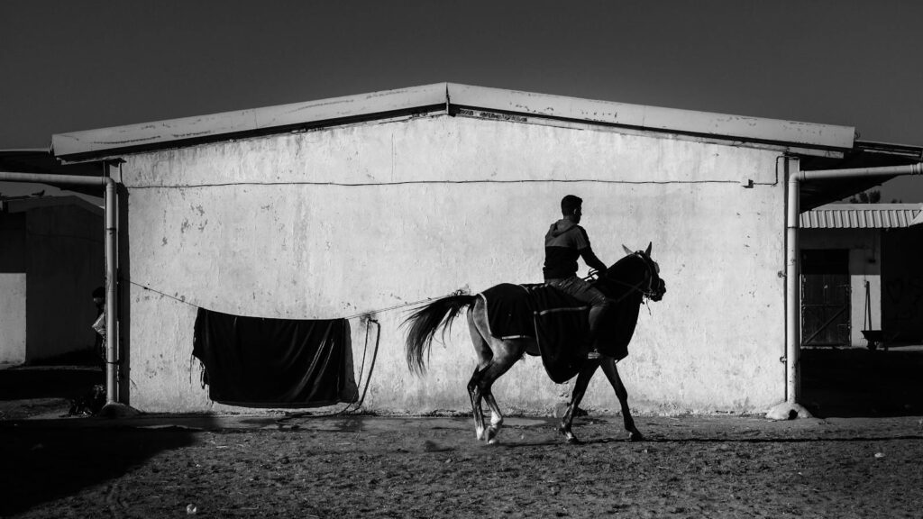 Silhouetted man on horse against barn in a dramatic black and white scene.
