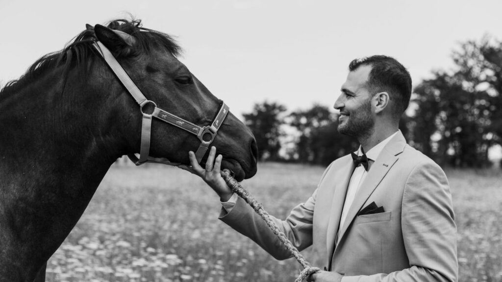 A man in a suit gently interacts with a horse in an open field, evoking harmony and elegance.