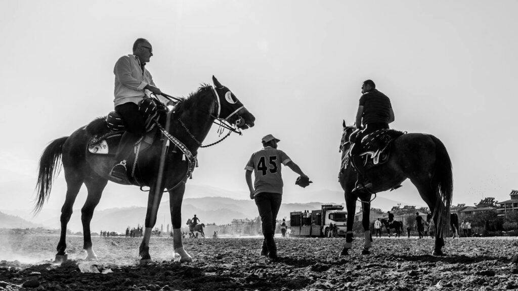 Black and white photo of horse riders and their horses during a daytime equestrian event in Salihli, Türkiye.