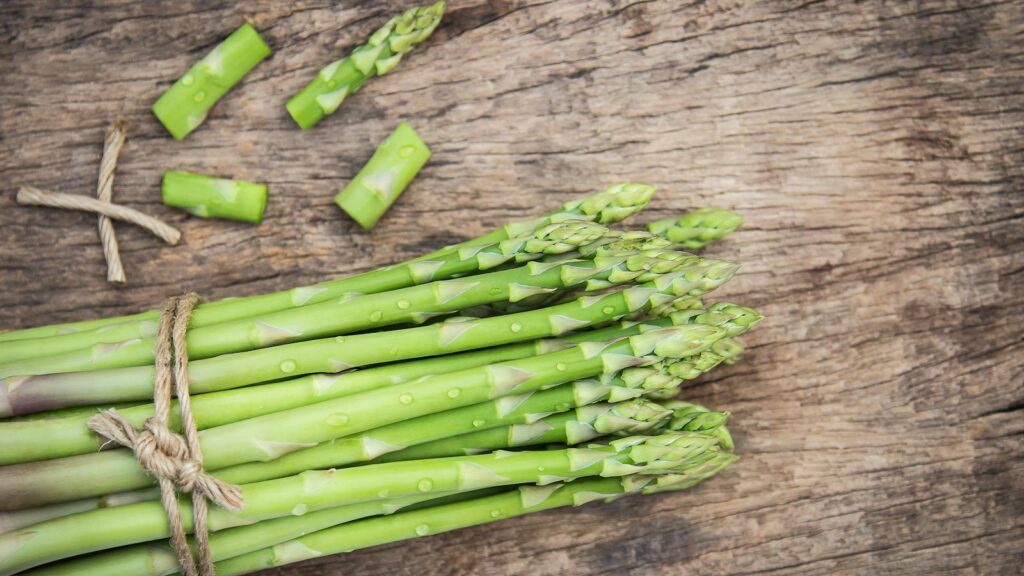 Bundle of fresh organic asparagus on a rustic wooden table, showcasing vibrant green colors and natural texture.