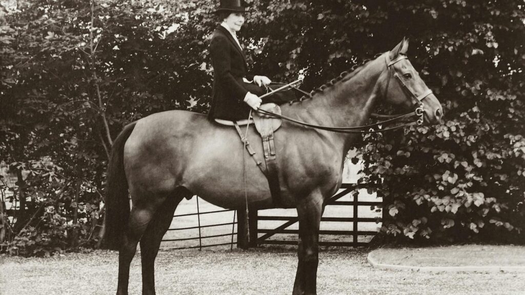 Classic sepia-toned photo of a woman in traditional riding attire on a horse.