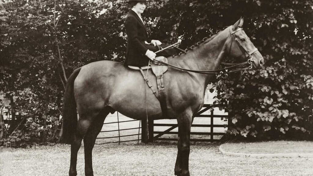 Classic sepia-toned photo of a woman in traditional riding attire on a horse.