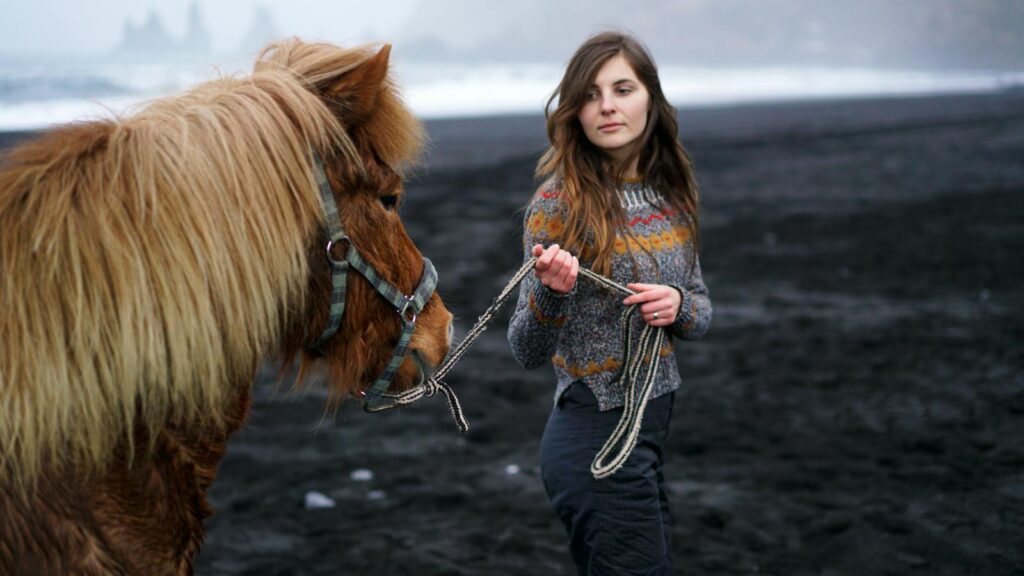 A woman leads a horse along a stunning black sand beach on a misty day.