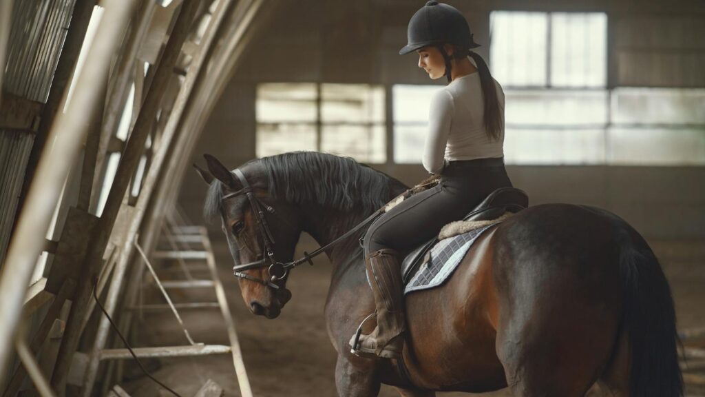 A young woman riding a horse indoors, dressed in equestrian attire, showcasing concentration and skill.