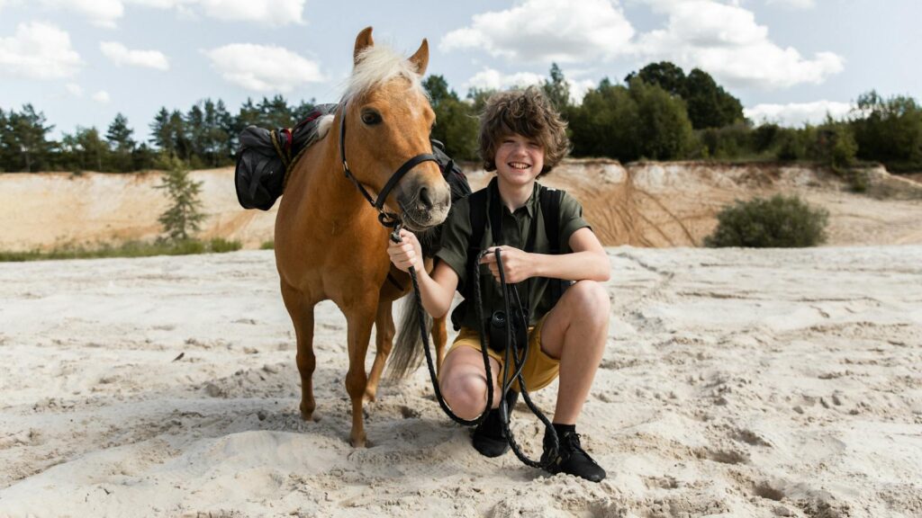Teenager with a pony enjoying a sunny adventure on a sandy landscape.
