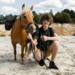 Teenager with a pony enjoying a sunny adventure on a sandy landscape.