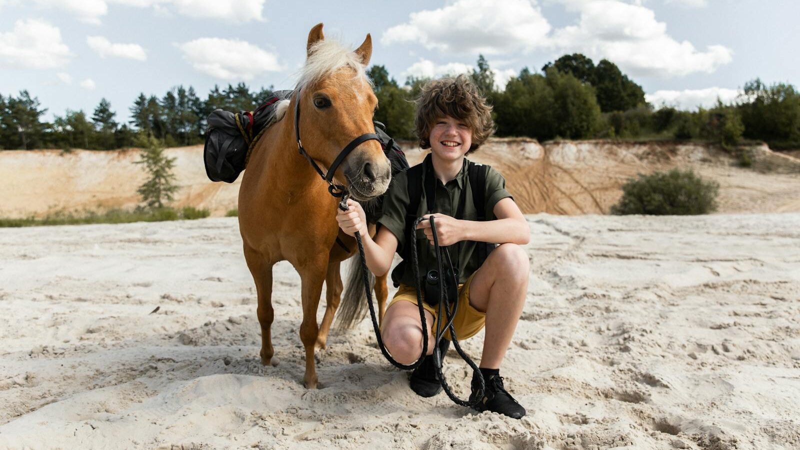 Teenager with a pony enjoying a sunny adventure on a sandy landscape.