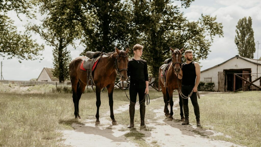 Two men with horses at a rustic stable, showcasing equestrian lifestyle.