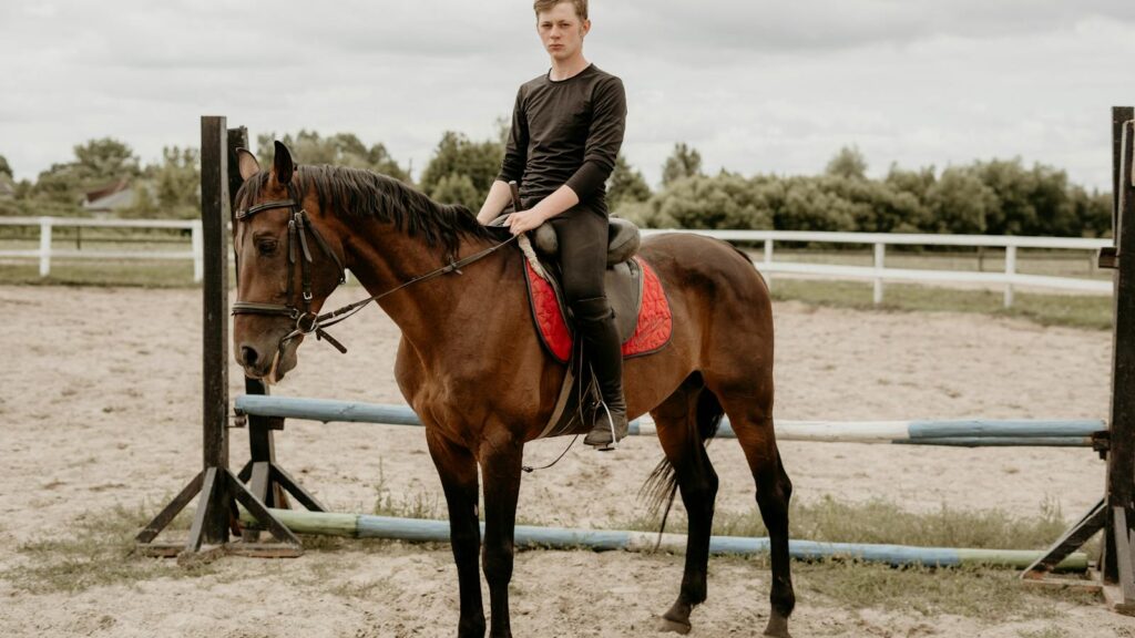 A young man sits confidently on a horse in an outdoor equestrian arena.