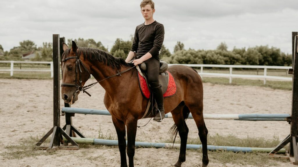 A young man sits confidently on a horse in an outdoor equestrian arena.