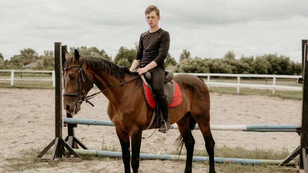 A young man sits confidently on a horse in an outdoor equestrian arena.