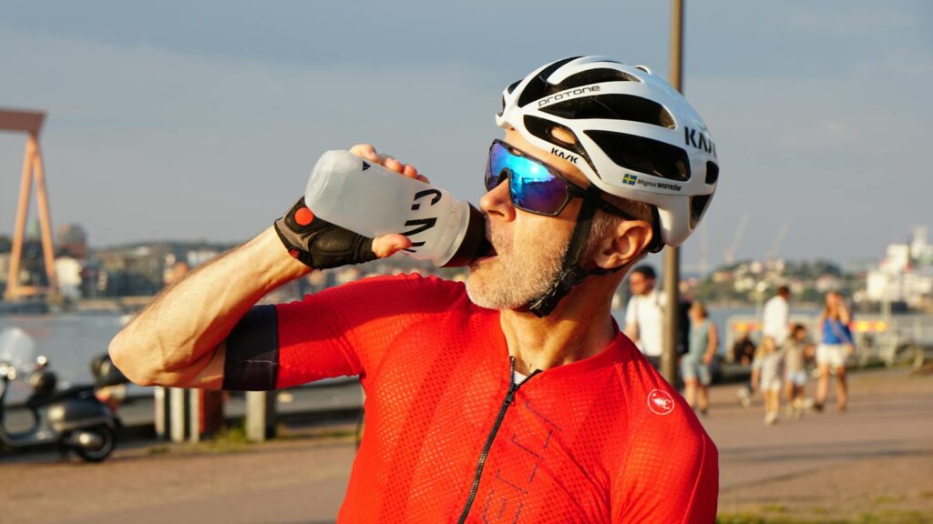 Male cyclist in red jersey drinking water outdoors, Gothenburg, Sweden.