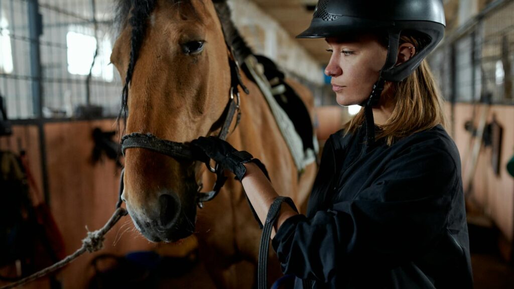 A woman in riding gear bonding with her horse inside a stable.