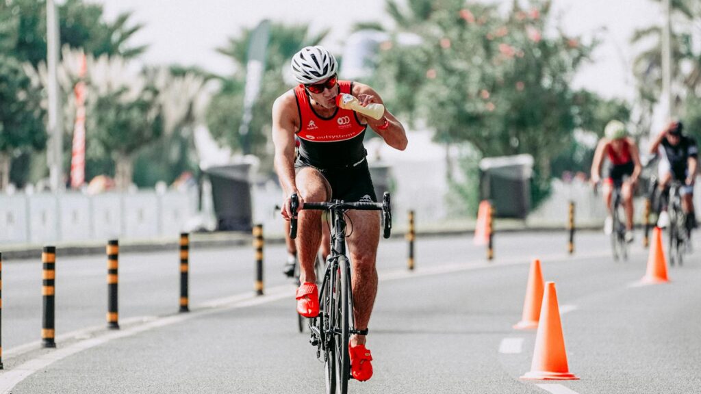 Full body of man in sportswear and helmet riding bicycle while drinking beverage during competition
