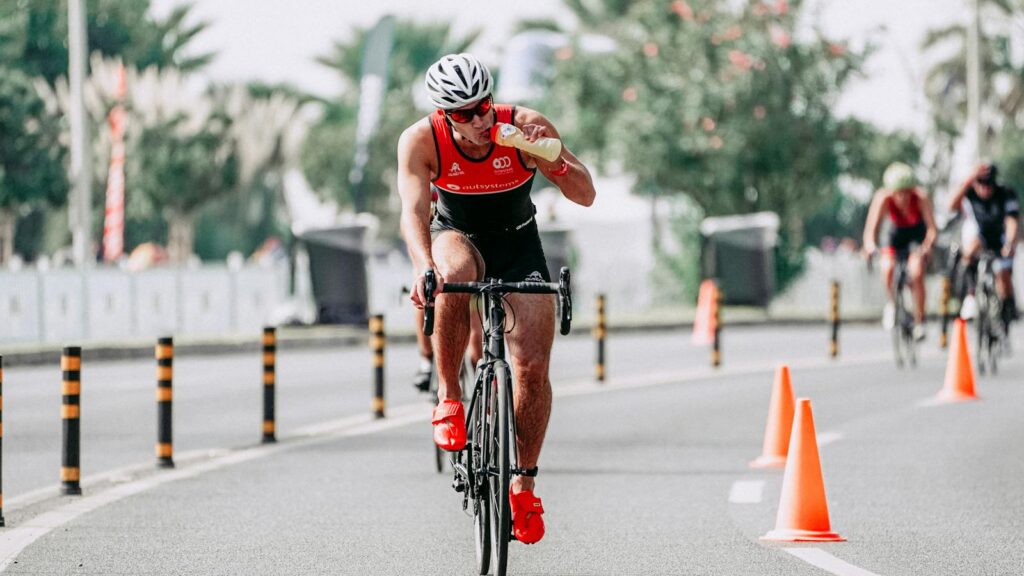 Full body of man in sportswear and helmet riding bicycle while drinking beverage during competition