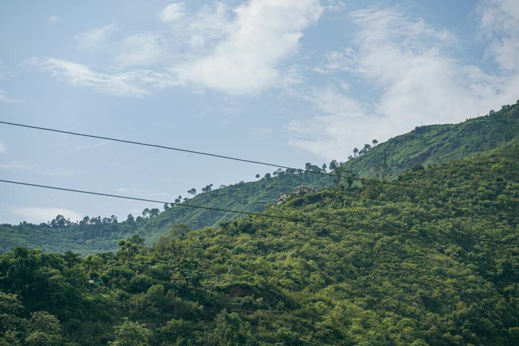 Lush green mountains with power lines under a bright blue sky, offering a stunning natural view.