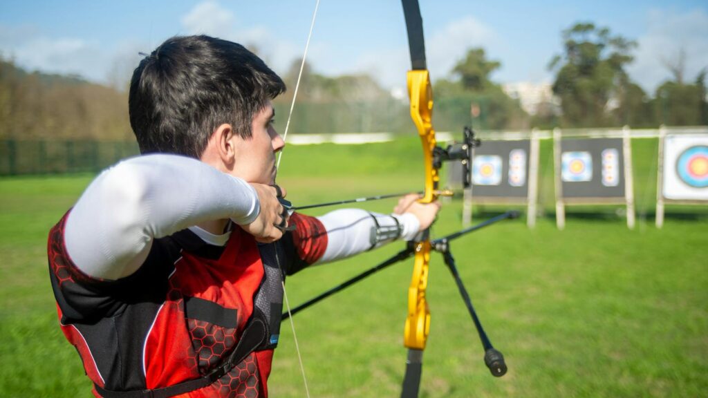 An archer aiming a bow at targets in an outdoor field on a sunny day.