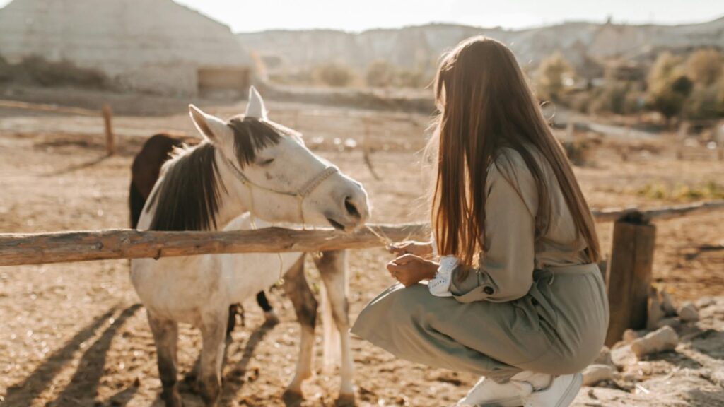 A woman feeding horses with unique rock formations in Cappadocia, Turkey in the background.