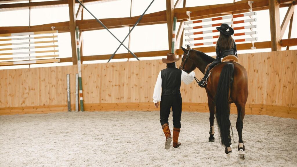 A girl riding a horse in an indoor arena with a man guiding them, both wearing cowboy hats.