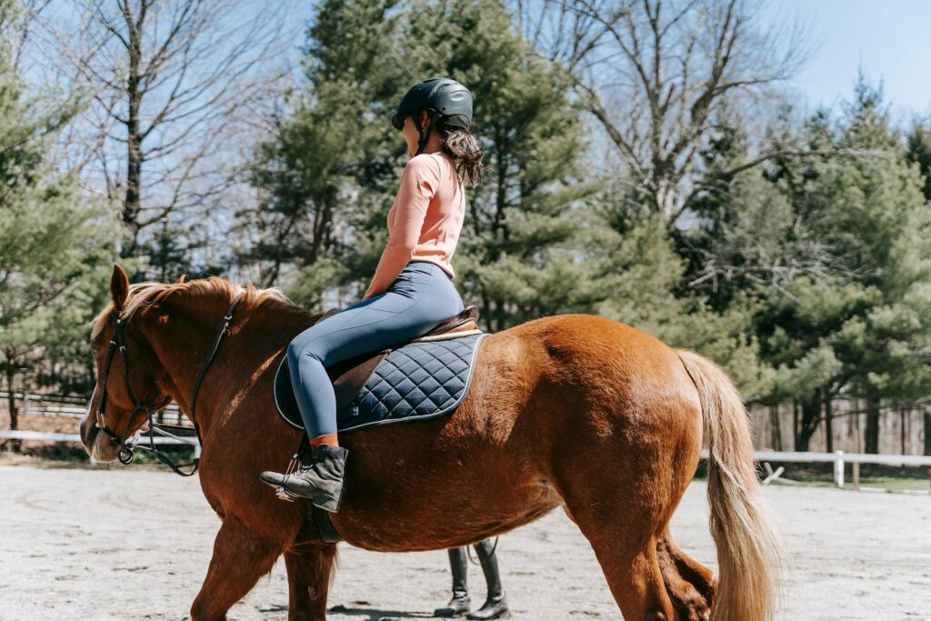 A woman rides a horse in nature, enjoying a sunny day outdoors.