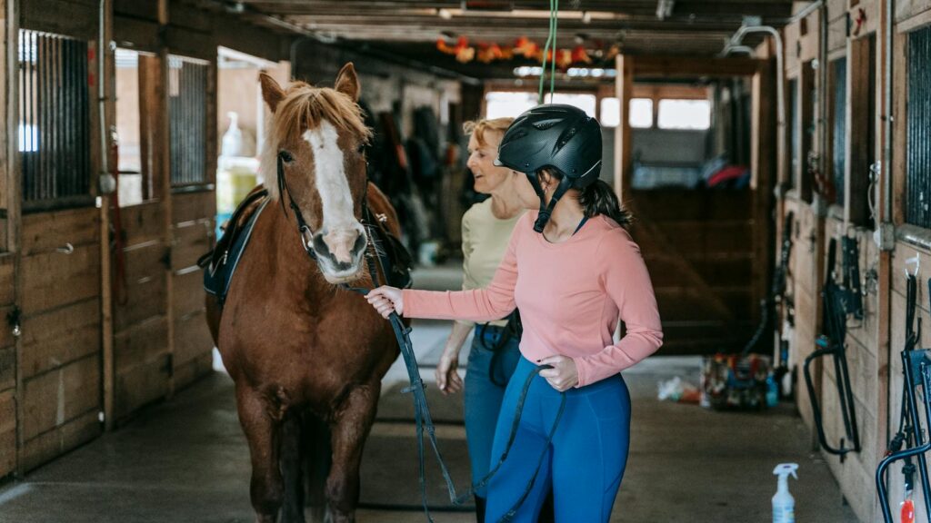 A beginner learning horseback riding under supervision in a stable.