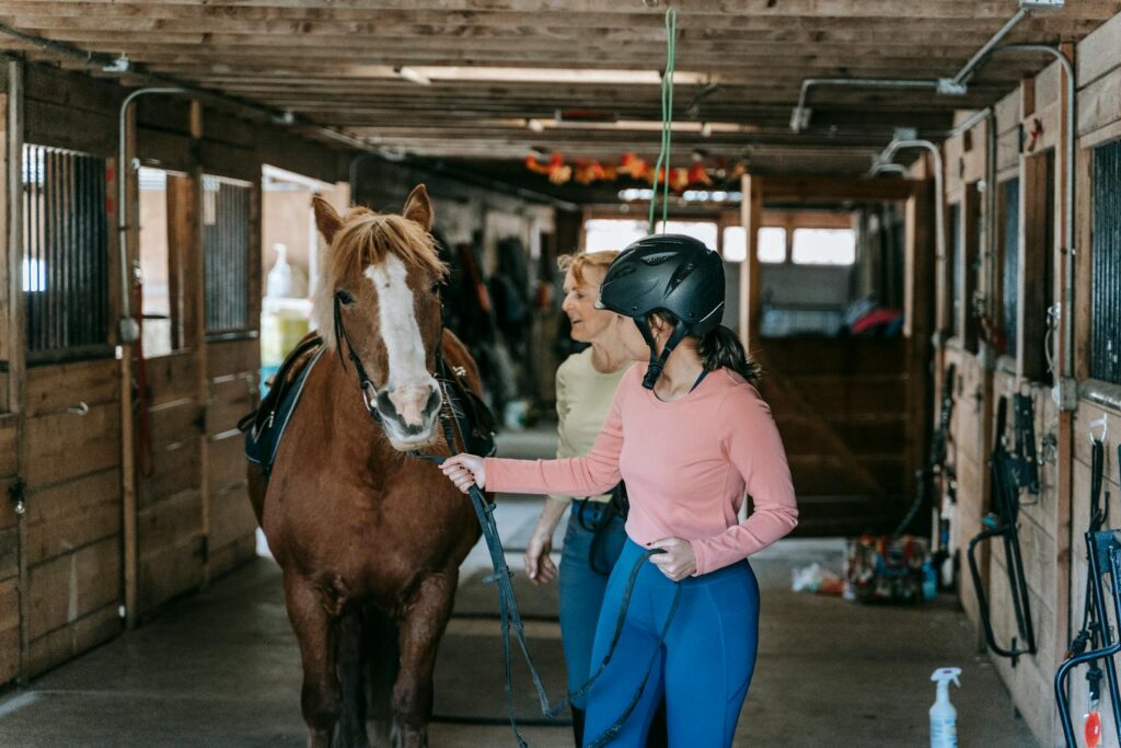 A beginner learning horseback riding under supervision in a stable.