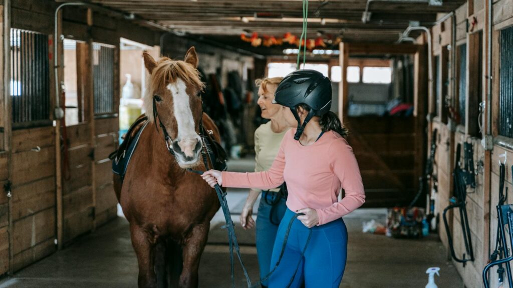 A beginner learning horseback riding under supervision in a stable.