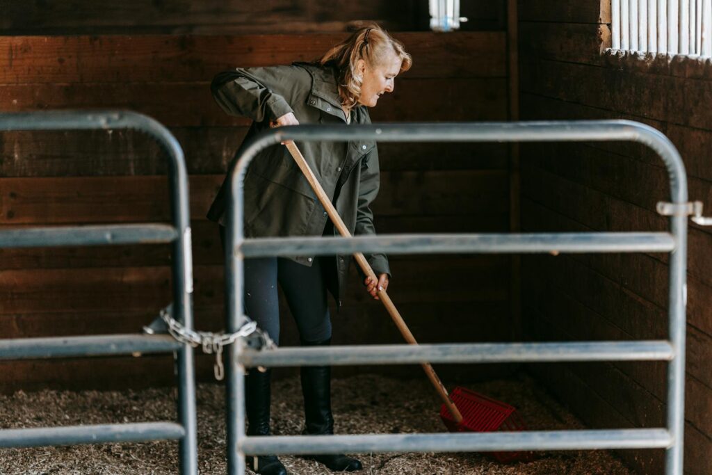 Adult woman cleaning a barn with a red broom, showcasing rural lifestyle activities.
