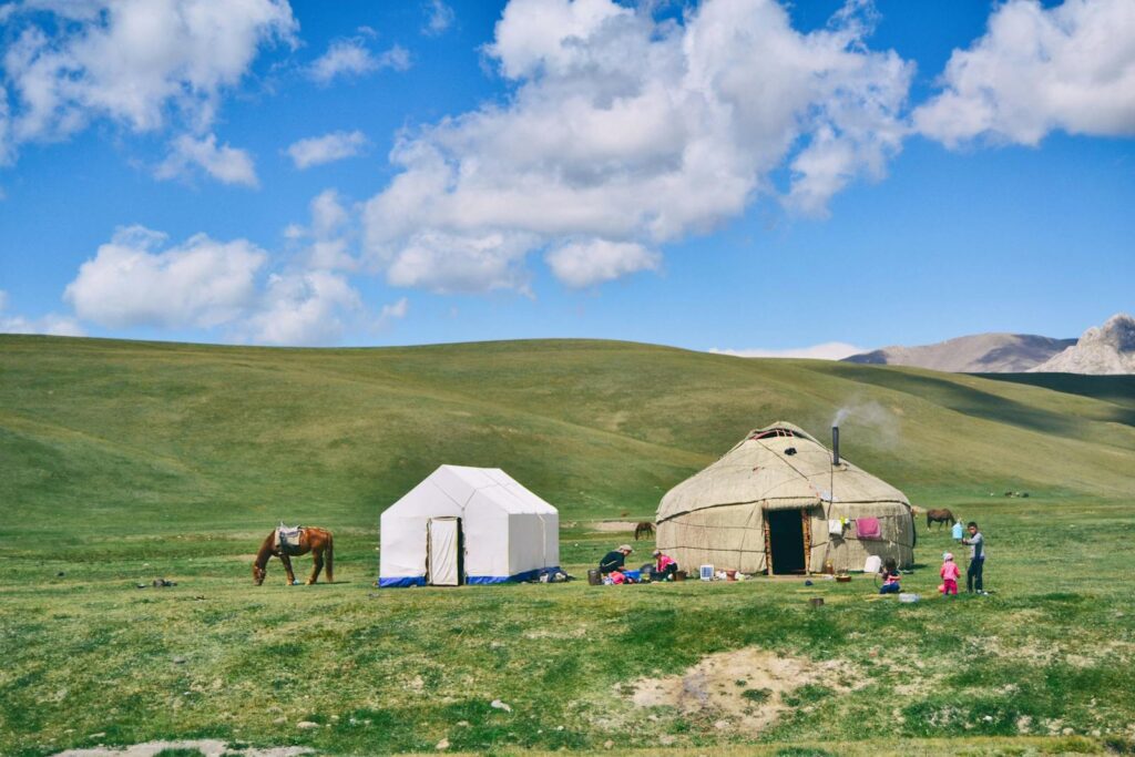 Serene rural landscape with a yurt, tent, and grazing horse under a blue sky.