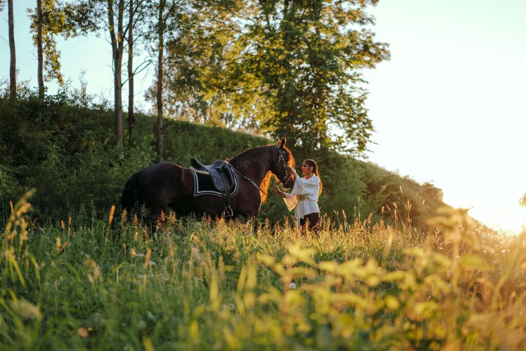 A woman standing with her horse in a green field during a warm sunset.