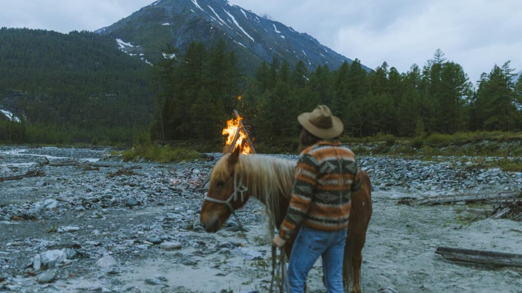 A lone camper with a horse by a bonfire in a mountainous landscape.