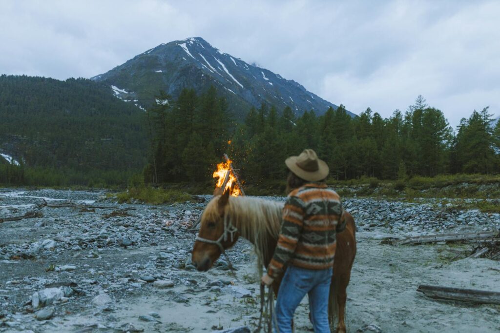 A lone camper with a horse by a bonfire in a mountainous landscape.