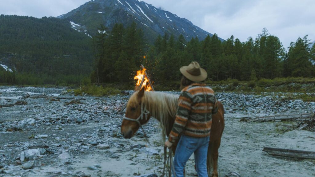 A lone camper with a horse by a bonfire in a mountainous landscape.