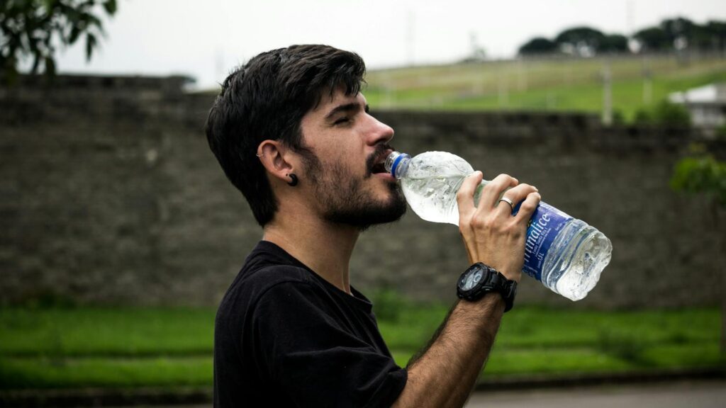 A young man drinks bottled water outside, staying hydrated and refreshed.