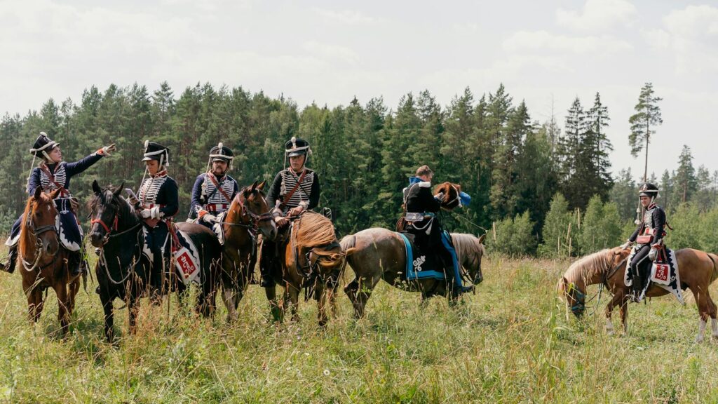 Group of soldiers on horseback in historical military uniforms during a reenactment outdoors.