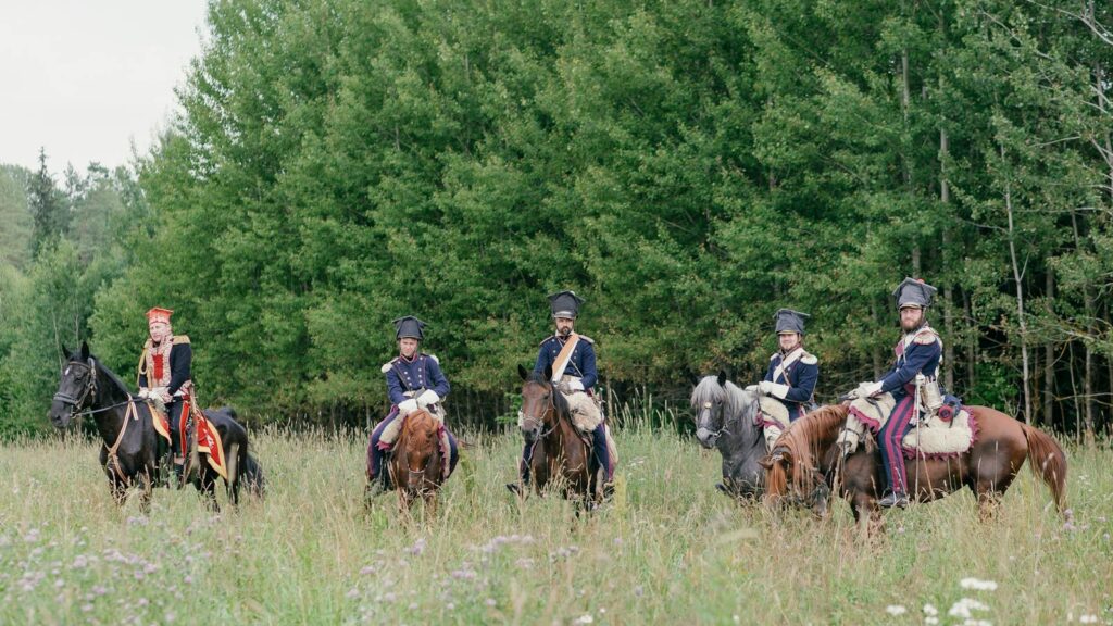 Group of men in military uniforms on horses during a historical reenactment in a meadow.