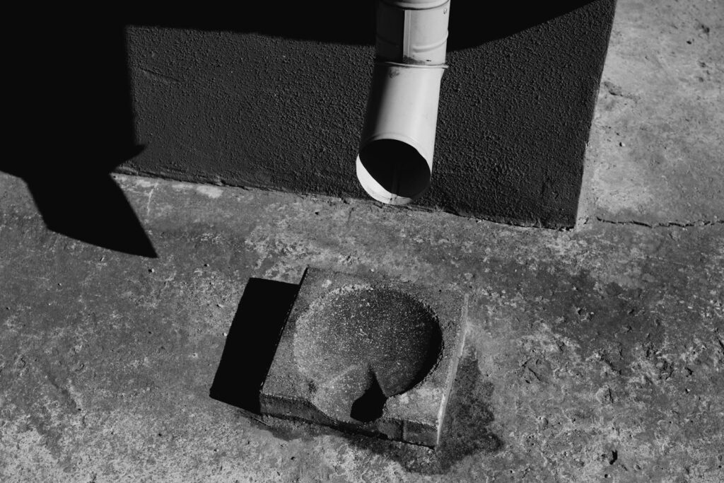 Black and white photo of a concrete drainage with sunlight casting shadows on pavement.