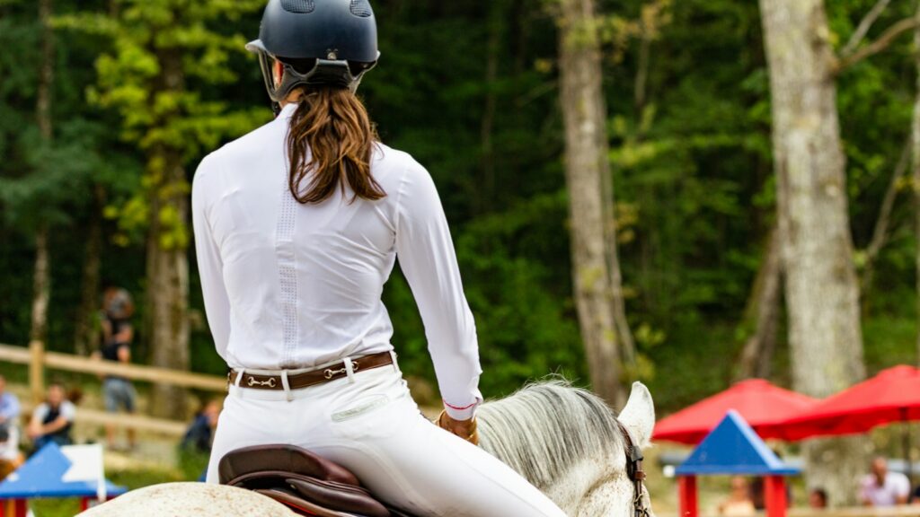 woman in white long sleeve shirt and brown skirt sitting on white horse during daytime