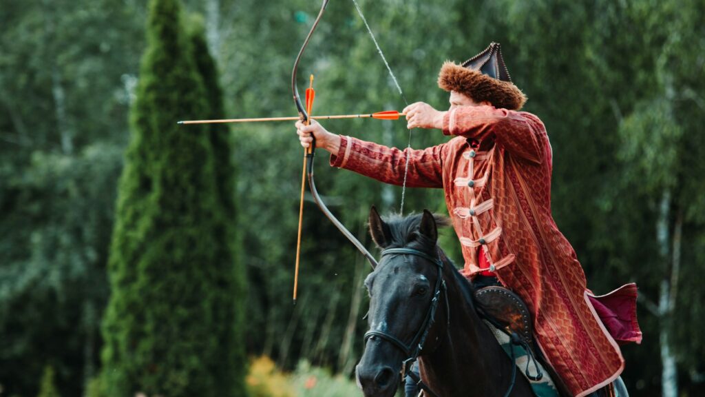 unknown person riding on black horse holding brown compound bow