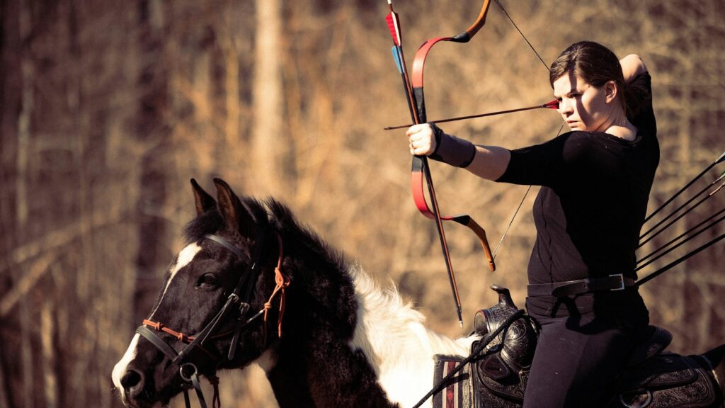 a woman riding on the back of a horse holding a bow and arrow
