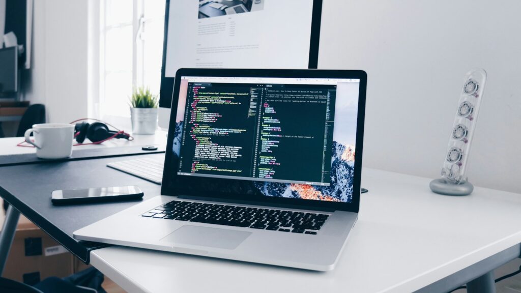 A MacBook with lines of code on its screen on a busy desk