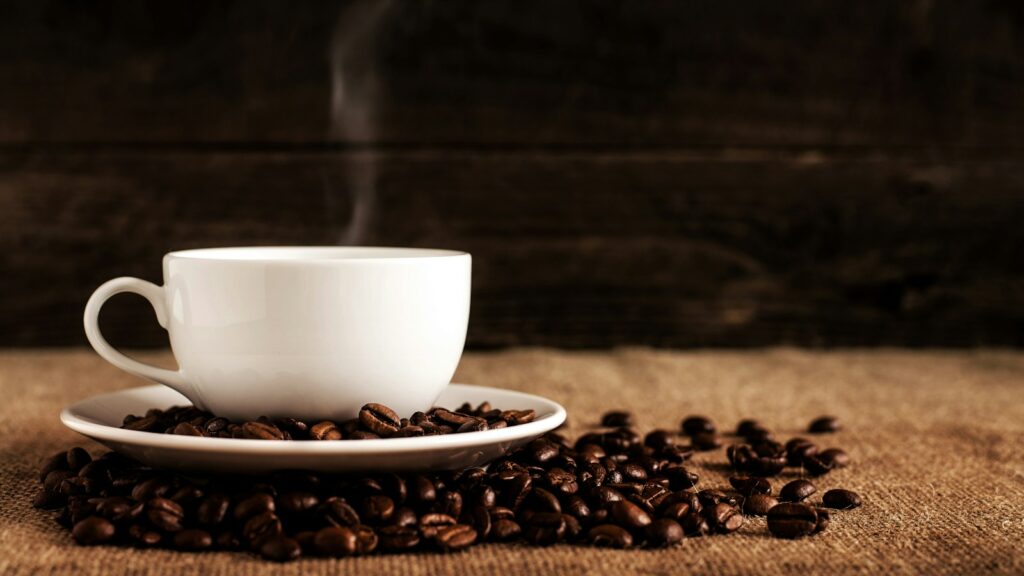 white ceramic mug and saucer with coffee beans on brown textile