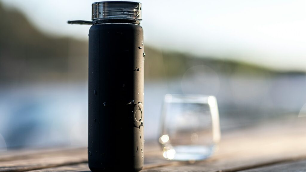 black bottle beside clear drinking glass on brown wooden table