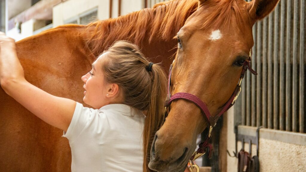 woman in white crew neck t-shirt standing beside brown horse during daytime