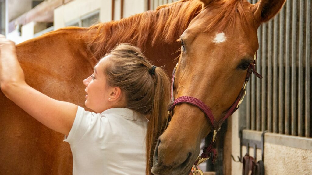 woman in white crew neck t-shirt standing beside brown horse during daytime